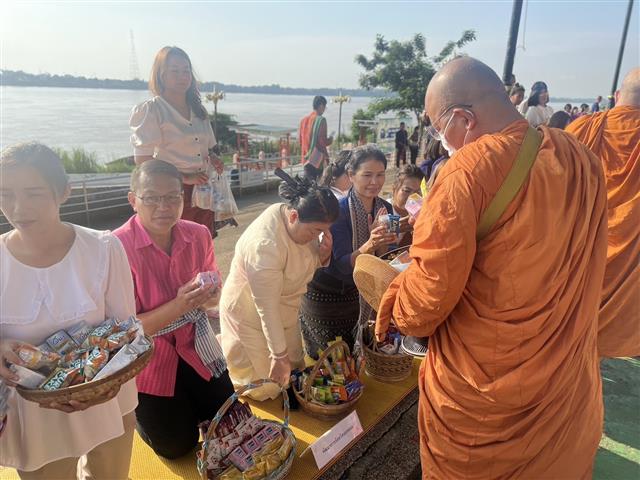 พช.นครพนม ร่วมใจพร้อมครอบครัวหิ้วตะกร้า ศรัทธาอิ่มบุญ อุดหนุนชุมชน : สวมผ้าไทย ห่มสไบ ใส่บาตรริมโขง