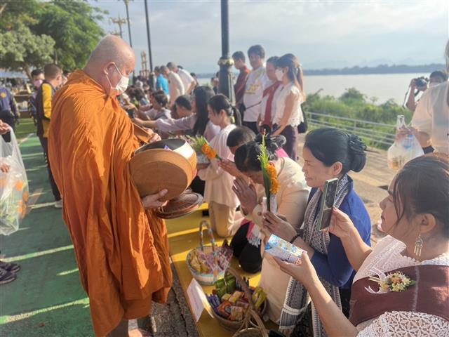 พช.นครพนม ร่วมใจพร้อมครอบครัวหิ้วตะกร้า ศรัทธาอิ่มบุญ อุดหนุนชุมชน : สวมผ้าไทย ห่มสไบ ใส่บาตรริมโขง
