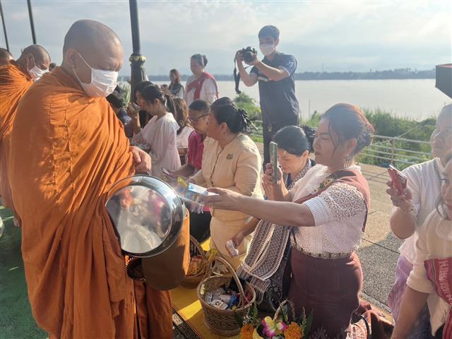 พช.นครพนม ร่วมใจพร้อมครอบครัวหิ้วตะกร้า ศรัทธาอิ่มบุญ อุดหนุนชุมชน : สวมผ้าไทย ห่มสไบ ใส่บาตรริมโขง