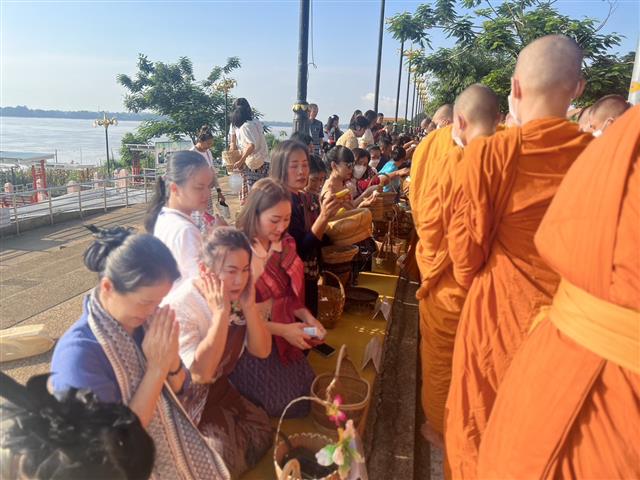 พช.นครพนม ร่วมใจพร้อมครอบครัวหิ้วตะกร้า ศรัทธาอิ่มบุญ อุดหนุนชุมชน : สวมผ้าไทย ห่มสไบ ใส่บาตรริมโขง