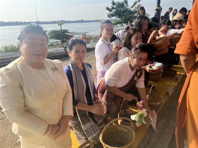 พช.นครพนม ร่วมใจพร้อมครอบครัวหิ้วตะกร้า ศรัทธาอิ่มบุญ อุดหนุนชุมชน : สวมผ้าไทย ห่มสไบ ใส่บาตรริมโขง